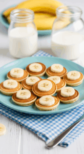Mini pancakes topped with banana slices served on a blue plate, with two glass jars of milk and fresh bananas in the background.