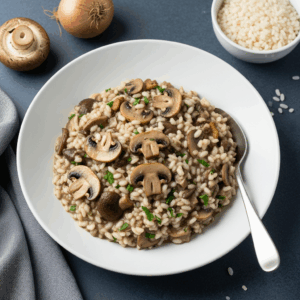 Mushroom risotto served in a white bowl, topped with sliced mushrooms and fresh herbs, with raw rice and onions in the background.